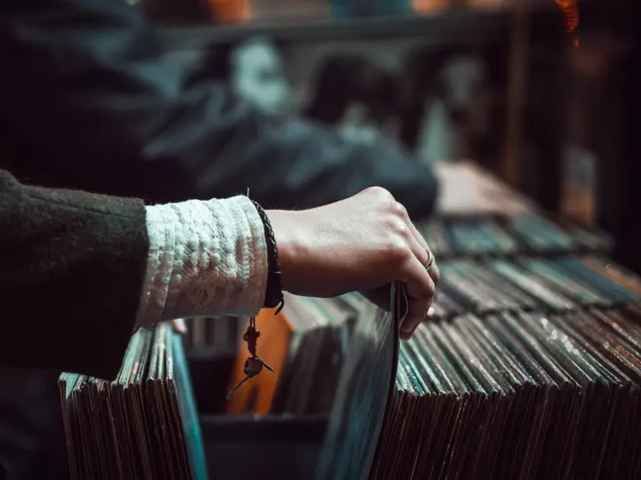 A hand with a woven bracelet pulling a record from a crate of sleeves.
